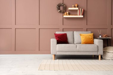 Kanepe, tabure, raflar ve kahverengi duvarın yanındaki sonbahar dekorasyonlarıyla oturma odasının içinde.