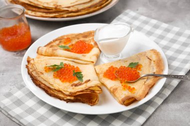 Kırmızı havyarlı leziz krepler ve grunge grisi arka planda bir kase ekşi krema.