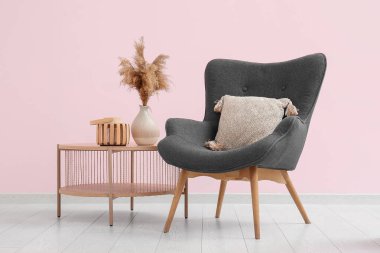 Pembe duvarın yanındaki sehpanın üzerinde pampa otu olan gri koltuk ve vazo.