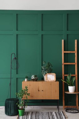 Yeşil duvarın yanında merdiven ve lamba olan ahşap dolap.