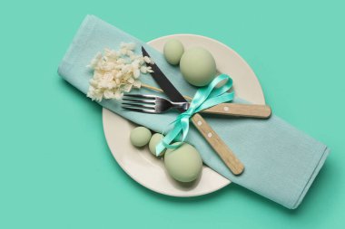 Renkli Paskalya yumurtaları, peçete ve turkuaz arka planda çatal bıçak seti olan şık bir masa.