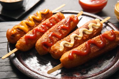 Siyah arka planda farklı soslu lezzetli mısırlı sosis tabağı.