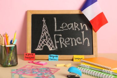 Tebeşir tahtasında LeARN FRENCH, Fransa bayrağı ve masa üzerinde kırtasiye