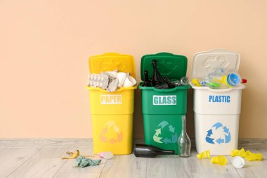 Bej duvarın yanında farklı türde çöp kutuları var. Geri dönüşüm kavramı