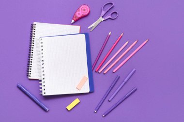 Defter, kalem ve makas mor arka planda. Üst görünüm