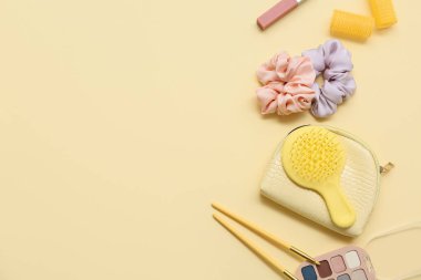 Sarı arka planda saç fırçası, bigudi ve ipek tokaları olan kozmetik çanta.