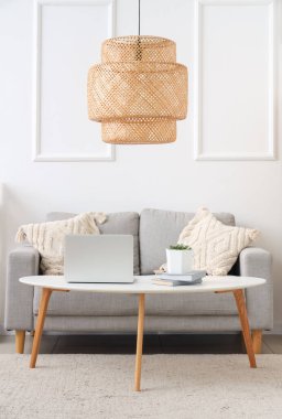 Stylish interior of living room with sofa and modern laptop on table