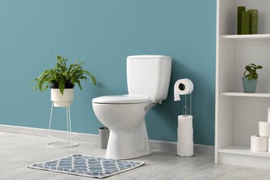 Tuvaletin içinde mavi duvarın yanında klozet ve bitki var.