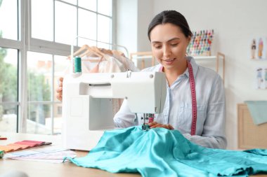 Atölyedeki masada kadın terzi dikiş dikiyor.