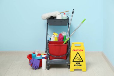 Temizlik malzemeleri ve mavi duvarın yanında uyarı levhası olan kapıcı vagonu.