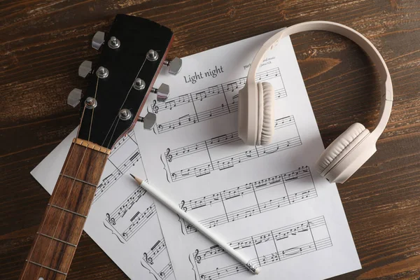 Müzik kağıtları, modern kulaklıklar, tahta arka planda kalem ve gitar, yakın plan.