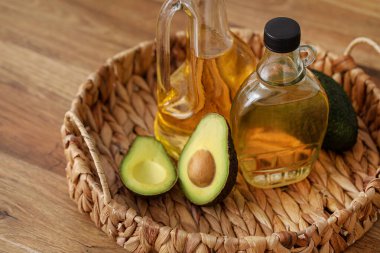 Taze yağ şişeleri ve ahşap arka planda avokado dolu hasır tepsi.