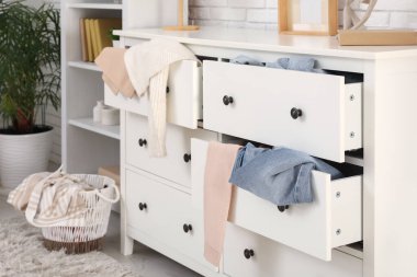 Oturma odasındaki beyaz tuğla duvarın yanında dağınık giysilerle tuvalet.