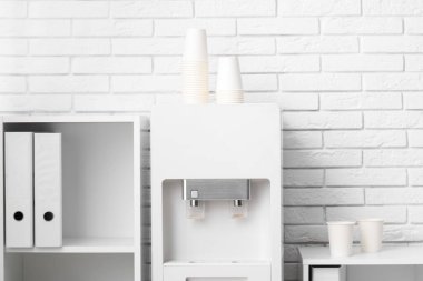 Modern su soğutucusu ve raf üniteleri beyaz tuğla duvarın yanındaki hafif ofiste.