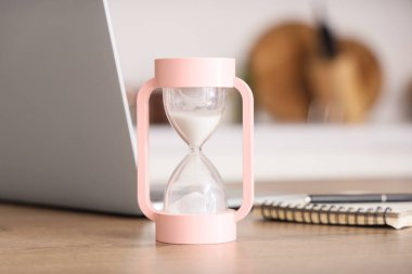 Kum saati, modern dizüstü bilgisayar ve defter odadaki masada.