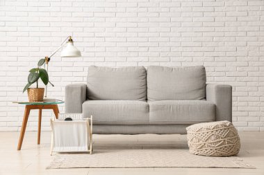 Oturma odasının içinde kanepe, lamba ve beyaz tuğla duvarın yanındaki masa.