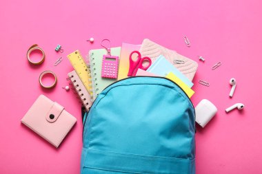 Mavi okul çantası, farklı kırtasiye malzemeleri ve pembe arka planda modern kulaklıklar.