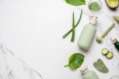 Kozmetik ürün şişesi, yüz masajı aletleri ve mermer arka plandaki malzemelerle kompozisyon