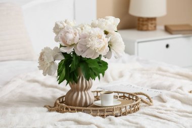 Vazoda şakayık çiçekli tepsi, bir fincan kahve ve yatağın üstünde kitap.