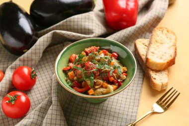 Bir kase sebze yahnisi, sarı arka planda bir dilim ekmekle servis edilir.