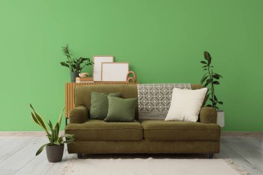 Yeşil duvarın yanında rahat kanepesi ve çiçekleri olan şık bir oturma odası.