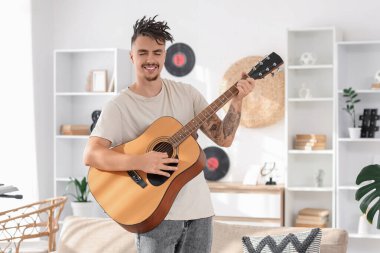 Young man with dreadlocks playing guitar at home