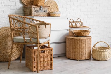 Şık oturma odasının içinde rattan koltuk, şifonyer ve farklı hasır sepetler var.