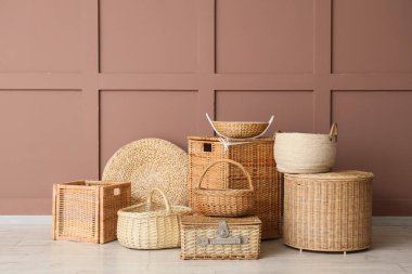 Kahverengi duvarın yanında farklı hasır sepetler.