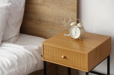Yatak odasındaki rahat yatağın yanında çalar saati olan şık bir komodin.