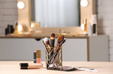 Ahşap masadaki fırçalı farklı makyaj ürünleri bulanık arka planda