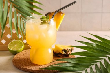 Bir bardak taze ananas suyu saman, kireç ve tropikal yapraklarla fayans duvarında