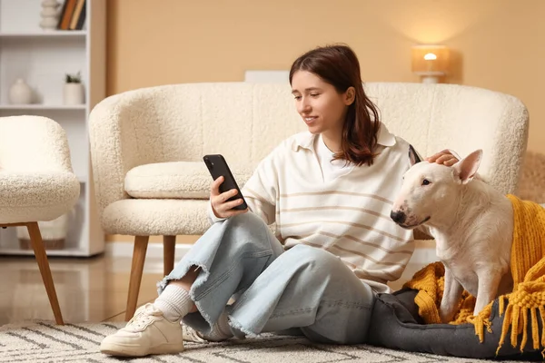 Cep telefonu kullanan genç bir kadın ve evde ekoseli tatlı Bull Terrier köpeği.