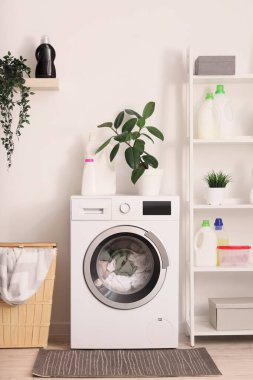 Çamaşır makinesi, sepeti ve raf ünitesi olan çamaşır odasının içi.