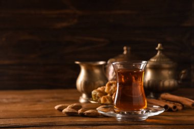 Tahta zemin üzerinde tarçın çubukları ve bademlerle bir bardak Türk çayı.
