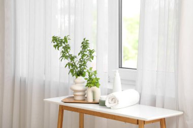 Havlu ve kozmetik ürünlerle çiçek açan vazolar şık bir tuvaletin penceresinin yanındaki masada.