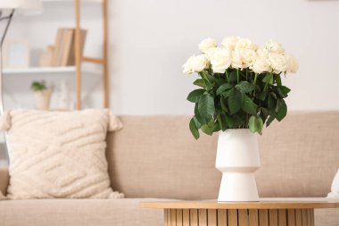 Oturma odasındaki masada beyaz güllü vazo.