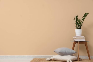 Bej duvarın yanındaki sehpada kitap ve bitki yığını var.