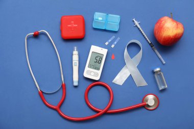 Kalemli glukometre, mavi arka planda gümüş farkındalık kurdelesi ve elma. Diyabet kavramı