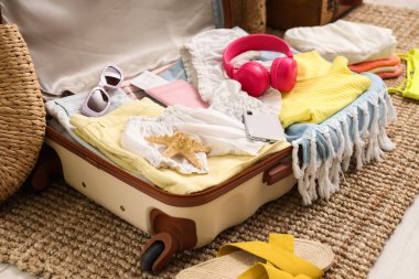 İçinde giysiler, plaj aksesuarları, kulaklıklar, cep telefonu ve pasaport bulunan bavulları yatak odasının yanında yere yakın.