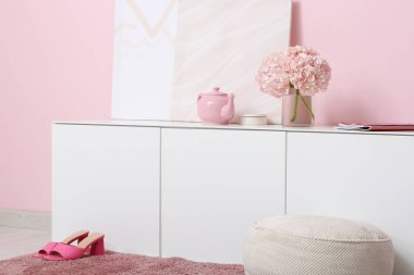 İçinde ortanca çiçekleri, çaydanlık ve pembe duvarın yanındaki resimler olan çekmeceler.