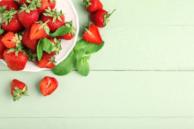 Yeşil ahşap zemin üzerinde taze çilek ve nane yapraklarıyla dolu bir tabak.
