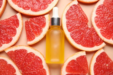Bir şişe kozmetik ürünü ve bej arka planda greyfurt dilimleri, yakın plan.
