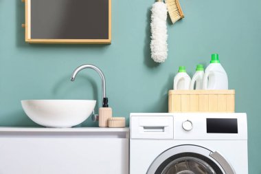 Modern çamaşır makinesi, içinde deterjan şişeleri olan sepet ve banyoda lavabosu olan çekmeceler, yakın çekim.