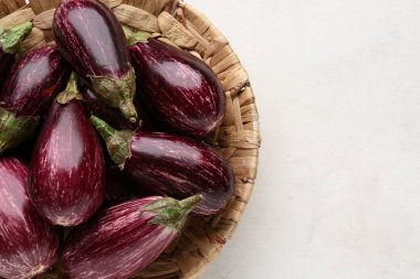 Beyaz arka planda taze olgun patlıcanlarla dolu bir hasır kase.