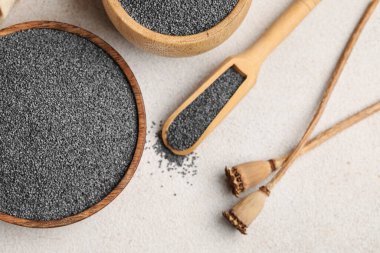 Tahta kaseler ve kepçeyle beyaz arka planda haşhaş tohumları