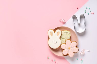 Plate with tasty Easter cookies and sprinkles on color background