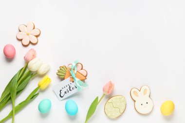 Beyaz arka planda lezzetli Paskalya kurabiyeleri, yumurtalar ve lale çiçekleri olan kompozisyon