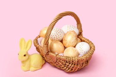Paskalya yumurtaları ve pembe arka planda tavşan heykelciği olan sepet.