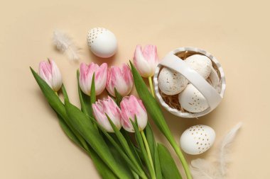 Paskalya yumurtalı sepet, bej arka planda tüyler ve laleler.