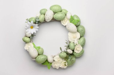 Beyaz çiçeklerden yapılmış Paskalya çelengi, yeşil boyalı yumurta ve açık arkaplanda kelebekler.